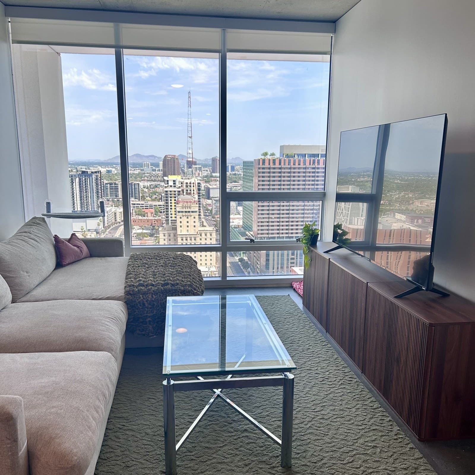 A high-rise living room cleaned by Spiff Pros — grey sectional, clear glass table, floor-to-ceiling windows overlooking the downtown Phoenix skyline in daylight
